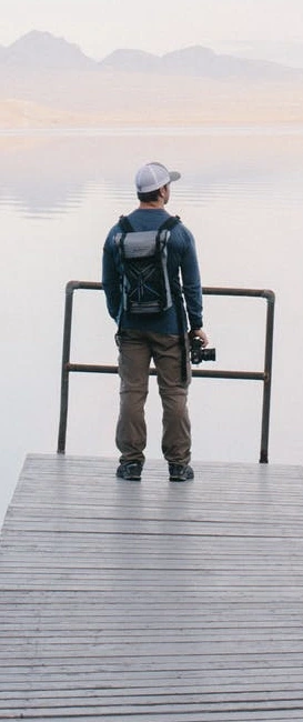 A man gazing at a calm lake with mountains in the background.