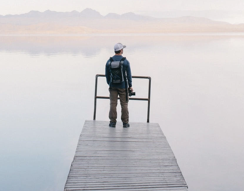  A man gazing at a calm lake with mountains in the background.