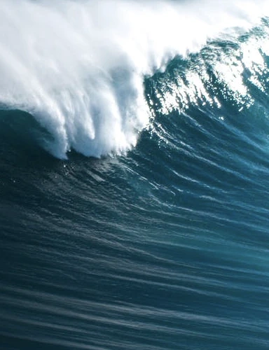 A massive wave crashing under a bright blue sky.